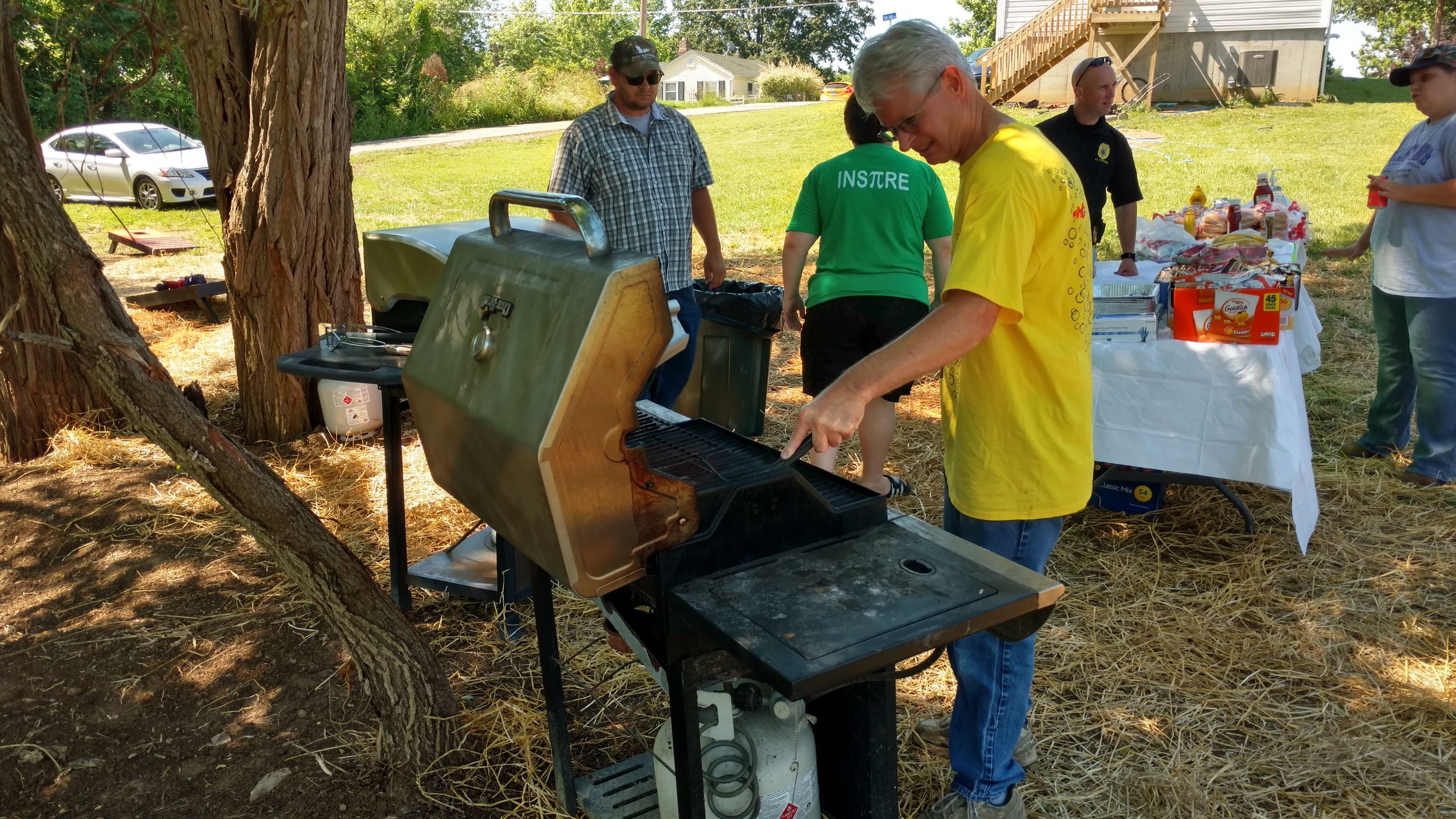 Man operating a grill while others talk and prepare food